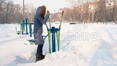 身穿蓝<strong>羽绒服</strong>，头罩的女人在城市的冬季公园里从事滑雪模拟器。